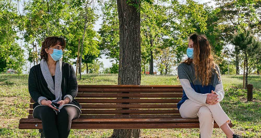 Personas usando cubrebocas sentadas en un banco respetando su distancia