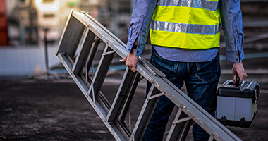 Trabajador con escalera de aluminio, caminando hacia una obra