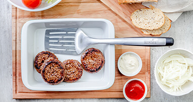 Plato con esptula y carne, recipientes con cebolla y aderezos
