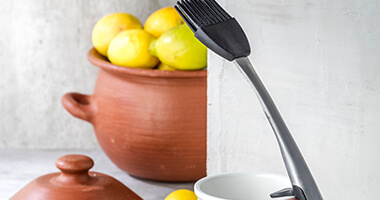 Brocheta para barnizar alimentos y olla con frutas al fondo