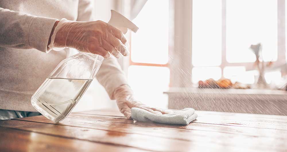 Persona limpiando una mesa de madera con un trapo limpio y alcohol