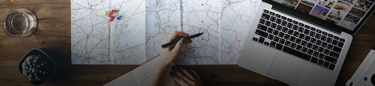 mano marcando en un mapa con laptop aun lado