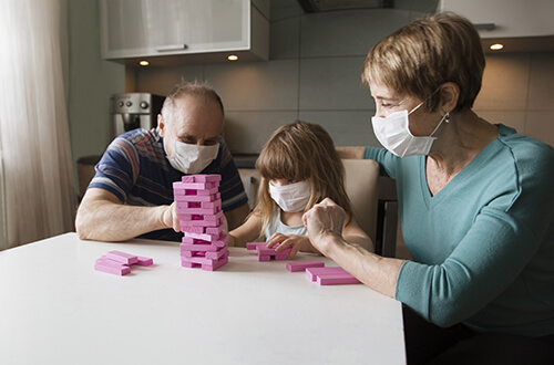 Familia jugando en casa y protegindose con cubrebocas