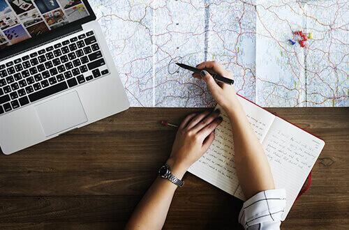 Mano marcando un mapa con una laptop a un lado