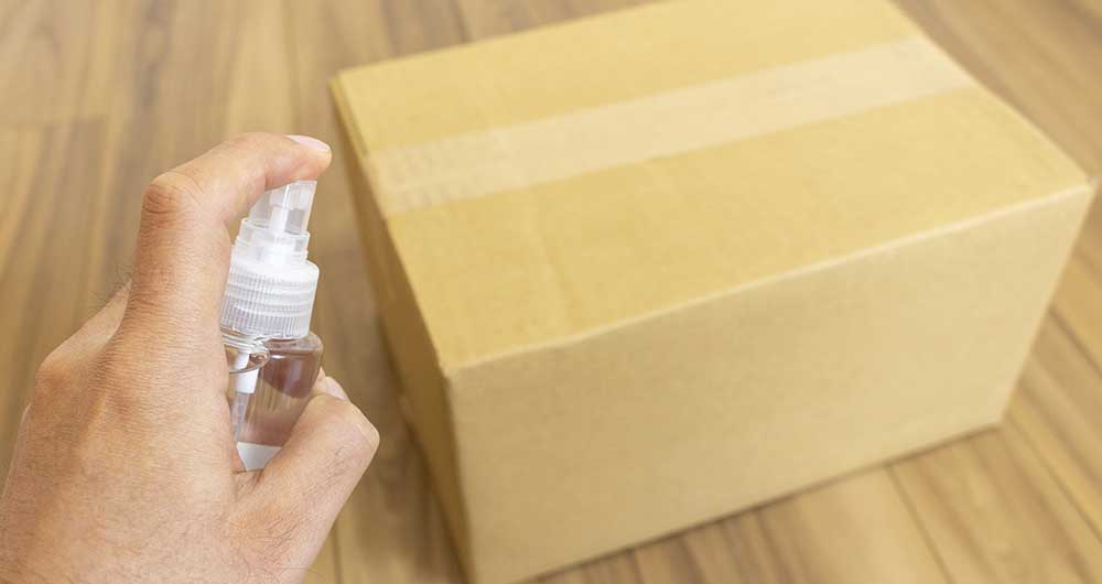 Mano con atomizador a punto de sanitizar una caja