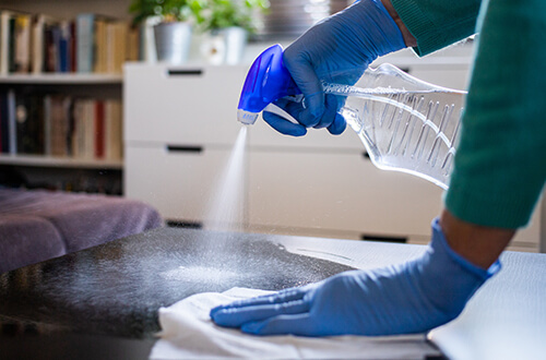 Persona con guantes de color azul limpiando una mesa