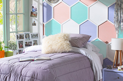 cama con sobrecama lila y fondo hexagonal de colores