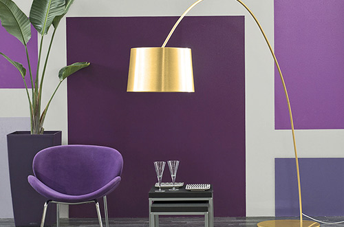 sala de estar con pared geométrica en violetas con silla moderna y lámpara dorada