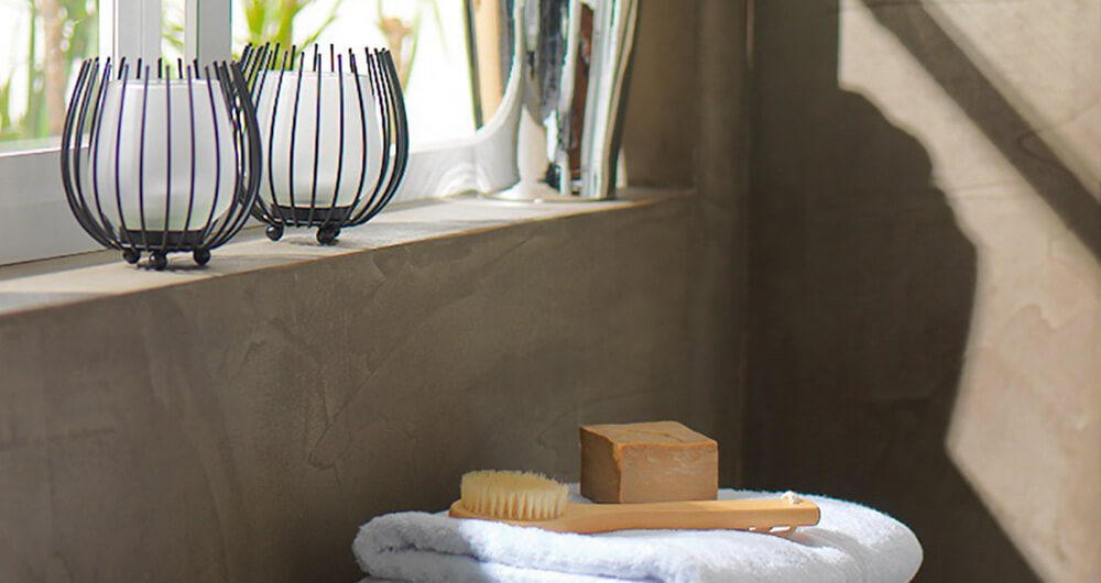 cepillo y jabn acomodados sobre toallas blancas, dobladas, en la esquina de un bao, con el reflejo de ventana